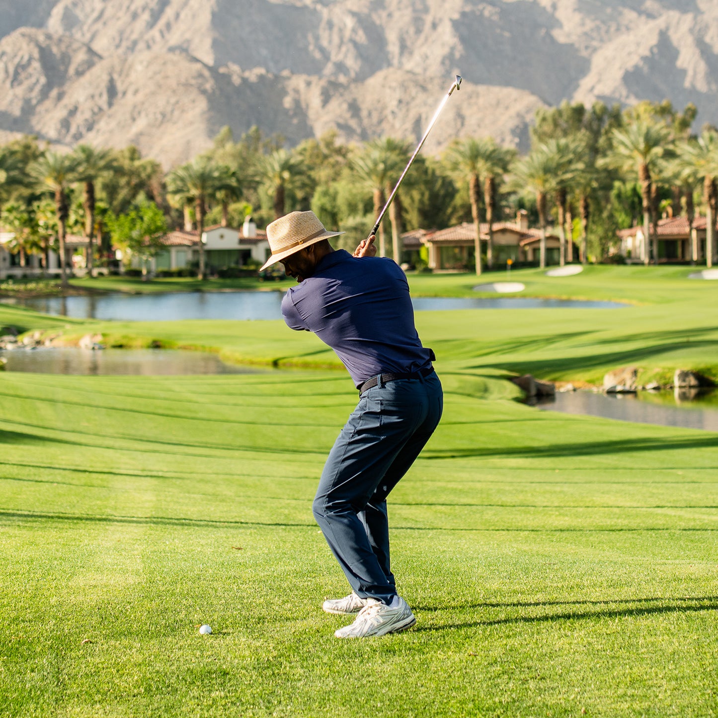 Golfer swinging a club on a golf course with mountains in the background wearing the Everett bamboo fedora, Mixed Camel