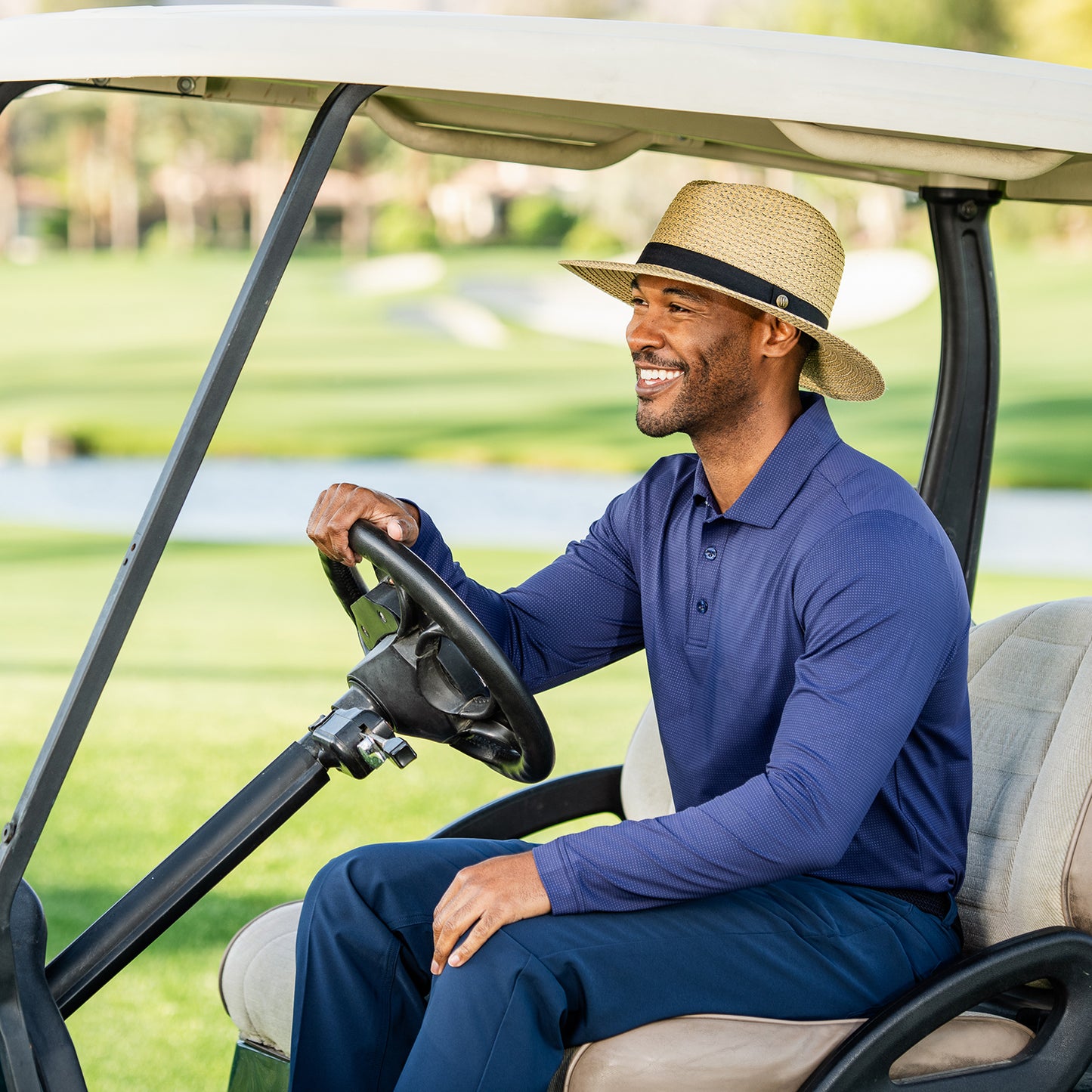 Man driving a golf cart on a golf course wearing the Palmer sun hat, natural