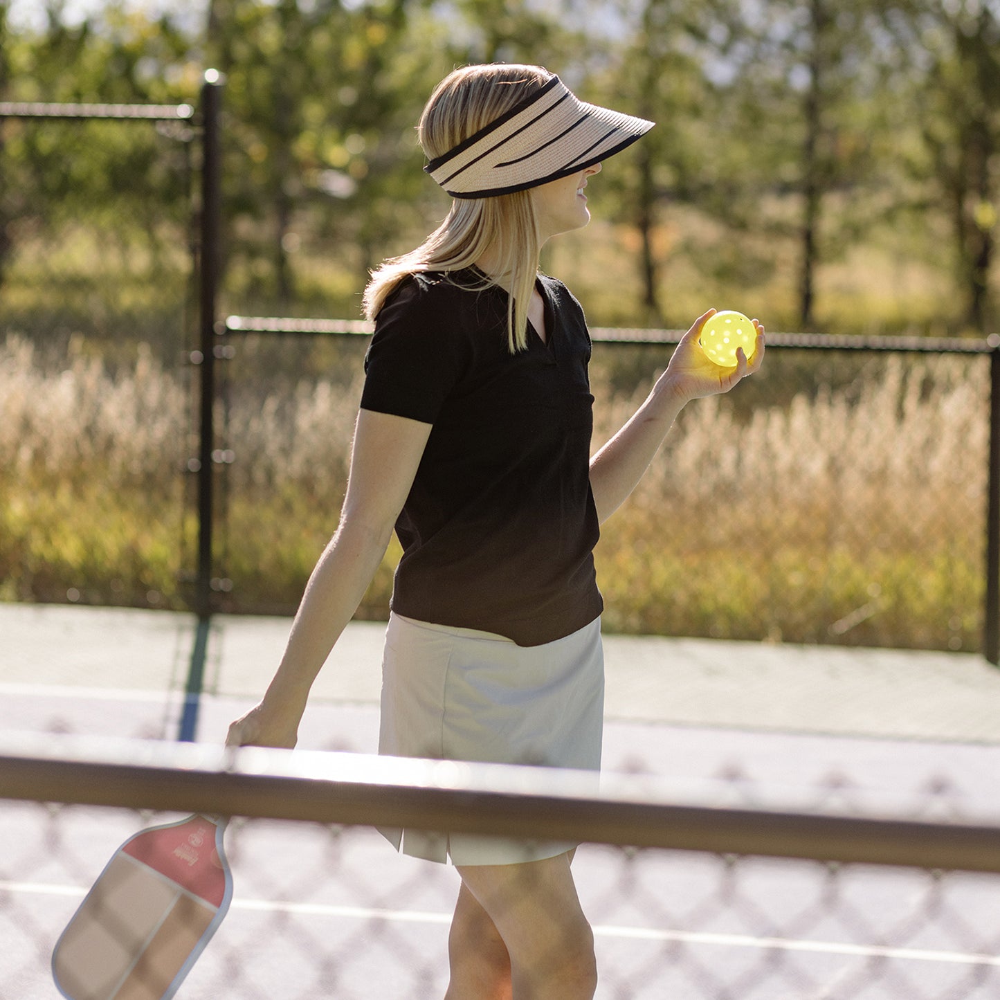 Woman enjoying a game of pickleball at a resort, shaded by the Wallaroo Savannah Wide Brim Sun Visor, designed for active sports and sunny summer afternoons, Camel/Black