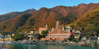 Temple in Uttarakhand, India, situated by a serene river, with devotees participating in vibrant ceremonies and rituals along the riverbank