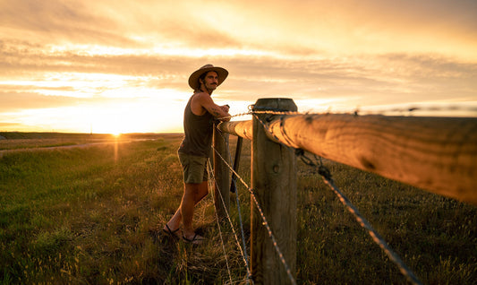 Man leaning on fence post at sunset wearing the artisan baja sun hat by Wallaroo