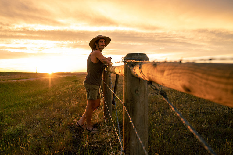 Man leaning on fence post at sunset wearing the artisan baja sun hat by Wallaroo
