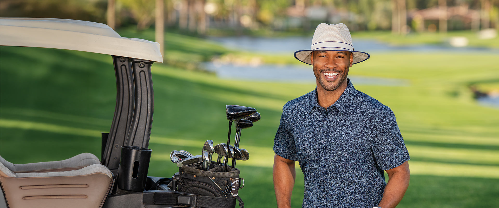 Man wearing Sterling fedora sun hat standing next to a golf cart on a golf course