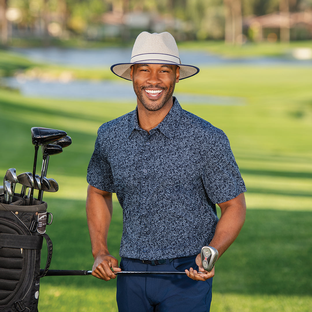 Man wearing Sterling fedora sun hat standing next to a golf cart on a golf course