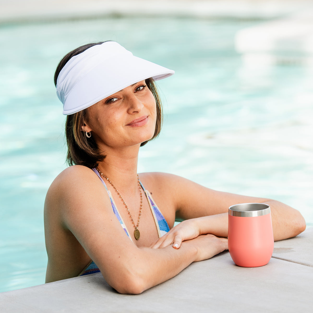 Woman in a bikini and Aqua Visor holding a pink tumbler by a pool, White