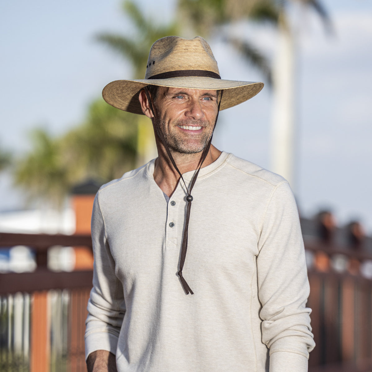 Man wearing the Baja UPF 50+ fedora sun hat in camel, with a dark brown band and chin strap, paired with a cream-colored long-sleeve henley shirt.   