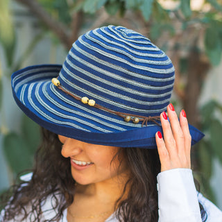 Woman wearing the Wallaroo Women's Navy Breton wide-brim sun hat, enjoying a sunny garden. Stylish UPF 50+ protection, travel-friendly, beach hat