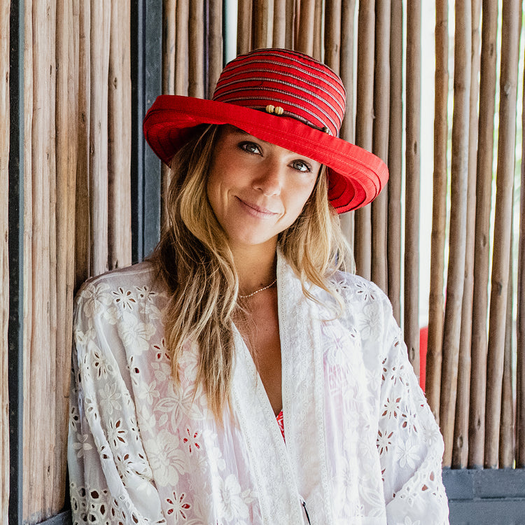 Woman wearing the Wallaroo Women's Red Breton sun hat, featuring a wide brim and UPF 50+ protection. Ideal for gardening, travel, and everyday outdoor sun safety with timeless style.