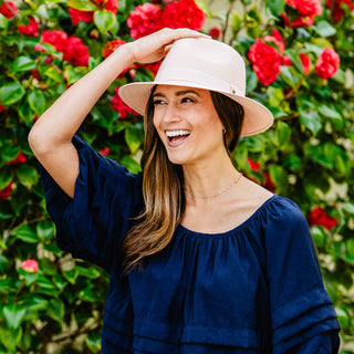 Woman wearing the Caroline packable SPF fedora sun hat, offering durable UV protection, stylish design, and a packable, travel-friendly feature for sunny days outdoors, Dusty Rose