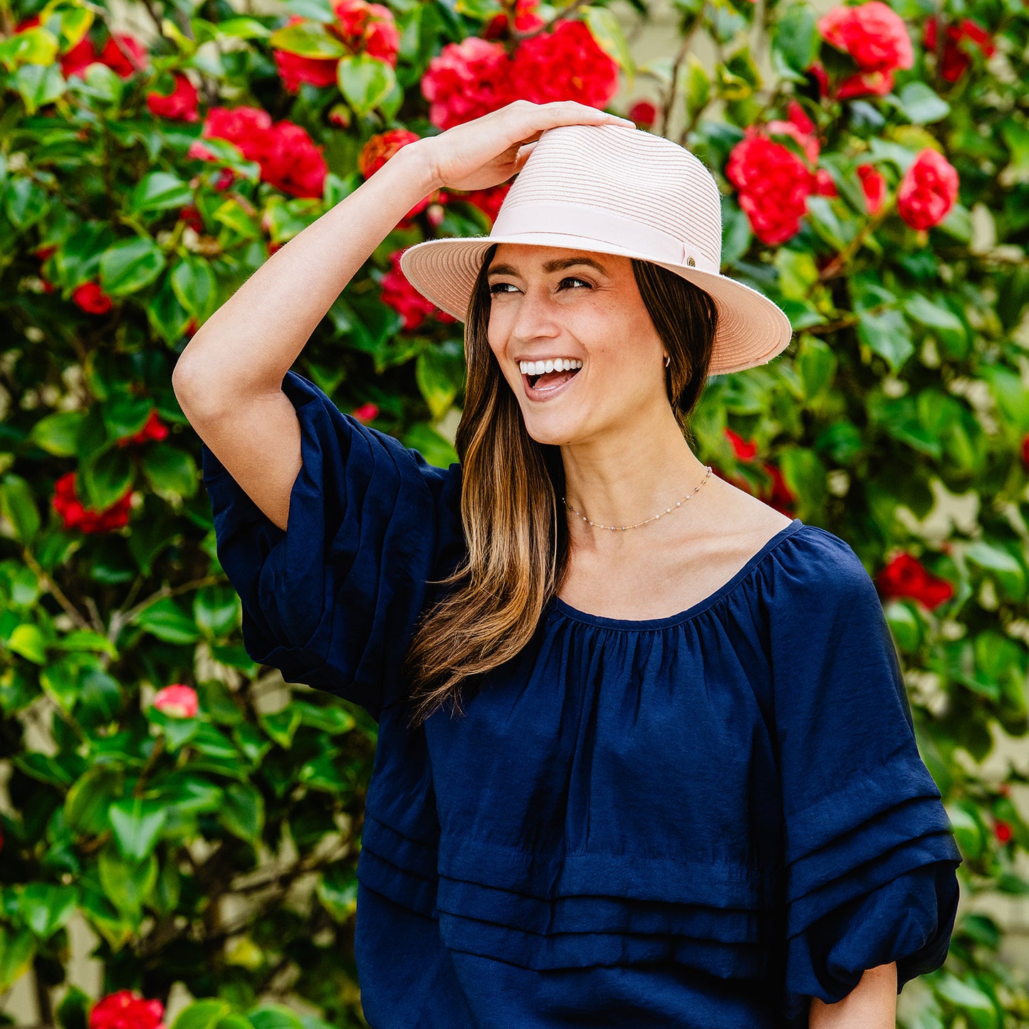 Woman standing in front of flowers in Wallaroo Caroline Fedora, stylish and functional sun protection, dusty rose
