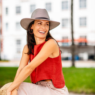 Woman wearing the Wallaroo Carter Wide Brim Fedora while sitting in a city park, offering stylish sun protection and UPF 50+ coverage for outdoor city adventures, Graphite