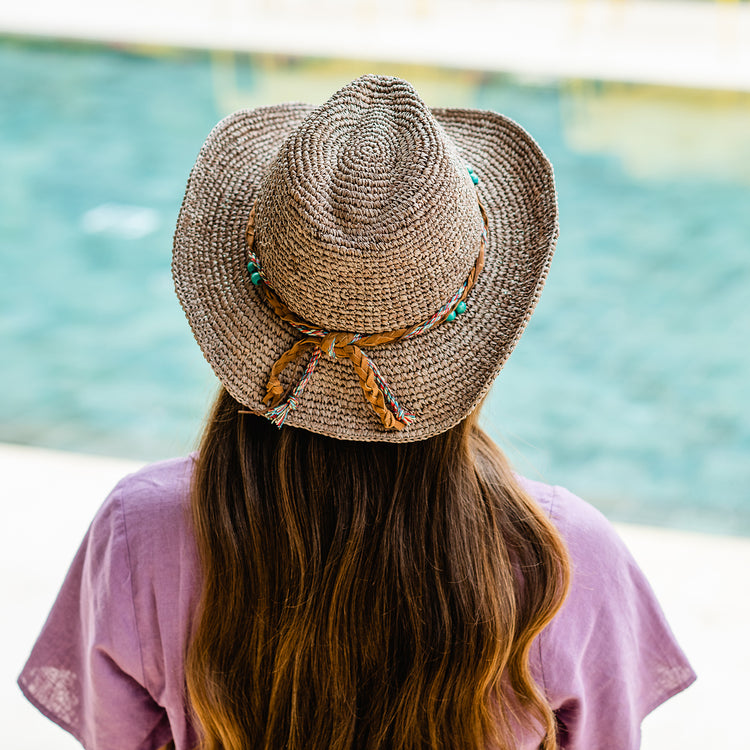 Woman in the Wallaroo Catalina Wide Brim Raffia Sun Hat walking along a beachside promenade, offering both style and sun protection for coastal adventures, Mushroom