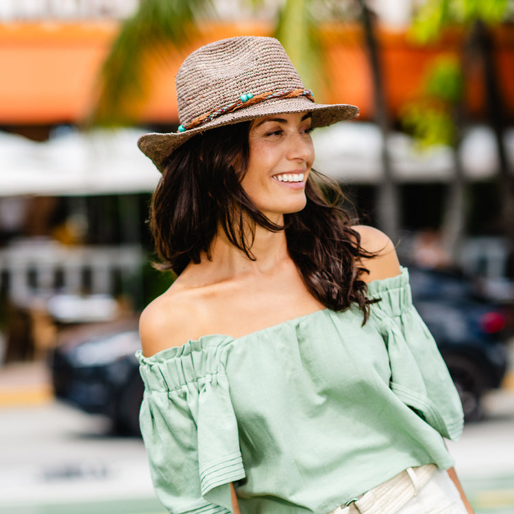 Woman relaxing wearing the Wallaroo Catalina Cowboy Crocheted Raffia Sun Hat, combining style and comfort for a sunny outdoor setting with sun protection, Mushroom