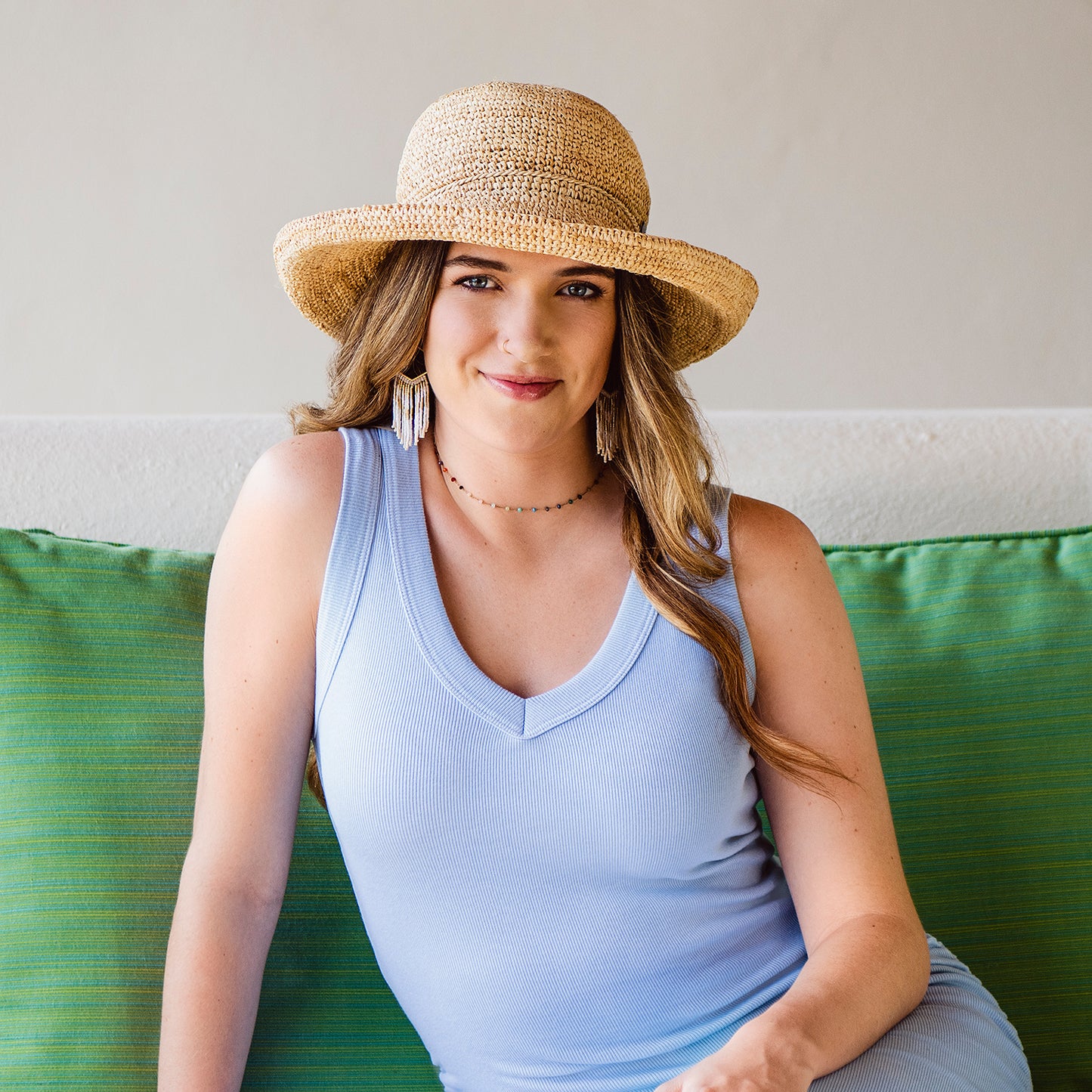 Woman wearing a Catalina raffia hat and light blue dress sitting on a green couch.