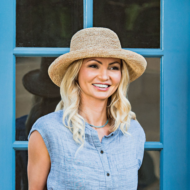 Woman wearing the Wallaroo Catalina Crocheted Raffia Sun Hat at a sunny outdoor café, offering a fashionable and functional way to protect from the sun during urban outings, Natural