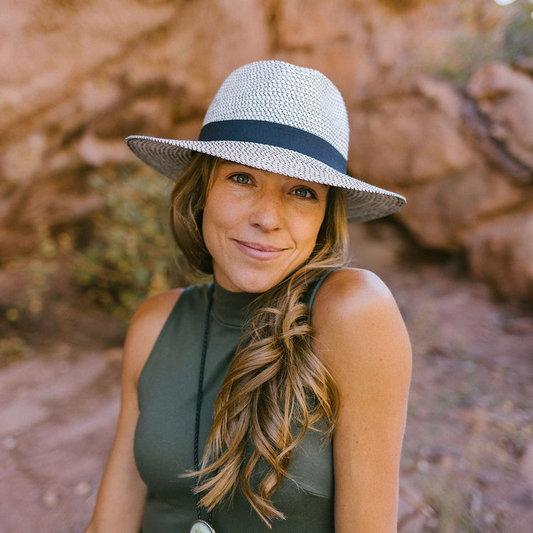 Person wearing the Wallaroo Unisex Charlie Wide Brim Fedora Sun Hat while walking through an urban park, offering UPF 50+ sun protection and timeless style for men and women, Ivory/Black