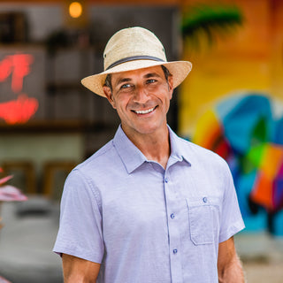 Man at a beachside café in the Wallaroo Cortez Panama Fedora, providing UPF 50+ protection and a fashionable wide brim design for sunny urban settings, Camel