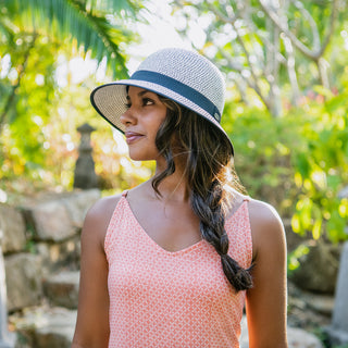 Woman strolling through a park in the Wallaroo Women’s Darby Wide Brim Cloche Sun Hat with a round crown, offering UPF 50+ sun protection and a stylish, timeless look, Ivory/Black