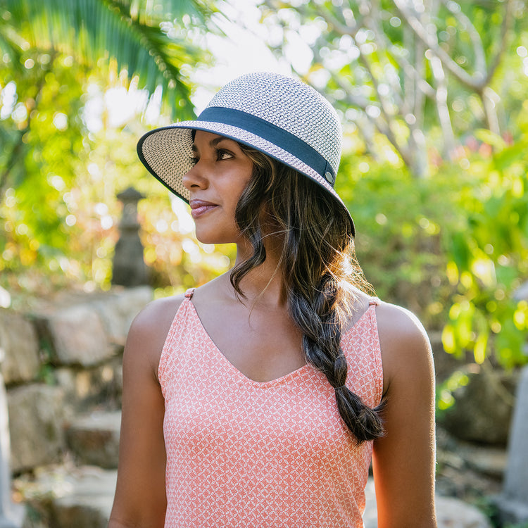 Woman strolling through a park in the Wallaroo Women’s Darby Wide Brim Cloche Sun Hat with a round crown, offering UPF 50+ sun protection and a stylish, timeless look, Ivory/Black