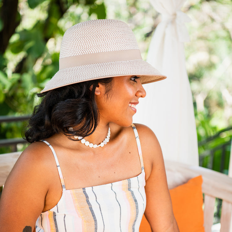 Woman enjoying an outdoor brunch wearing the Wallaroo Darby Wide Brim Cloche Sun Hat, featuring chic sun protection and a flattering design perfect for sunny urban settings, Ivory/Taupe