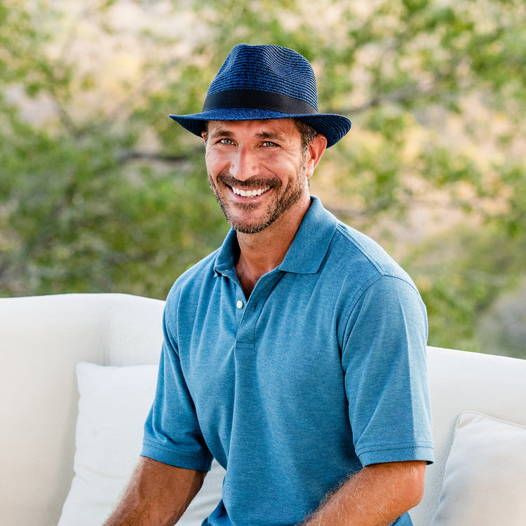 Man relaxing on a coastal terrace, wearing the Carkella Del Mar Trilby Fedora Sun Hat, ideal for keeping cool with breathable fabric during hot summer months by the beach, sale, 'Mixed Navy'