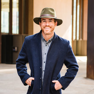 A person enjoying a mountain lodge patio, wearing the Wallaroo Durango Felt Fedora, a unisex hat with a classic design, ideal for active outdoor lifestyles, Olive