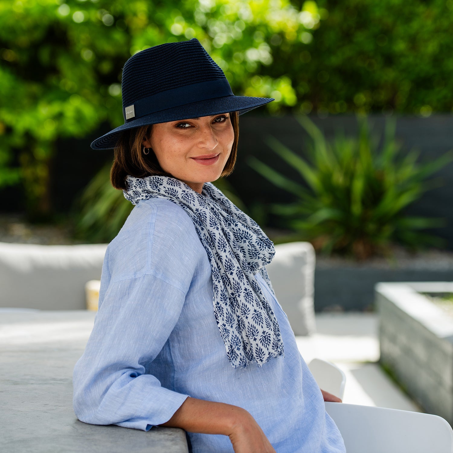 Woman wearing a blue shirt and Carkella Fairway fedora hat with a patterned scarf, sitting outdoors, Navy