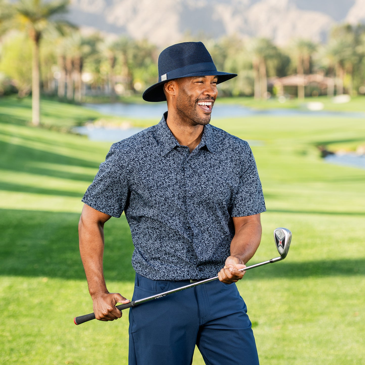 Man in Carkella Fairway fedora hat and shirt holding a golf club on a golf course, Navy