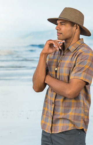 A man in a brown wide-brim fedora-style hat looking off in the distance on the beach.