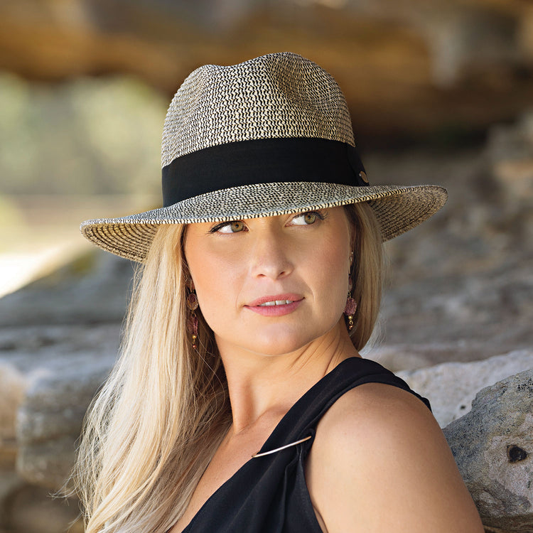 Woman strolling along a waterfront boardwalk in the Wallaroo Women's Josie Sun Hat, offering natural fiber construction and wide-brim sun protection for active outdoor experiences, Mixed Black