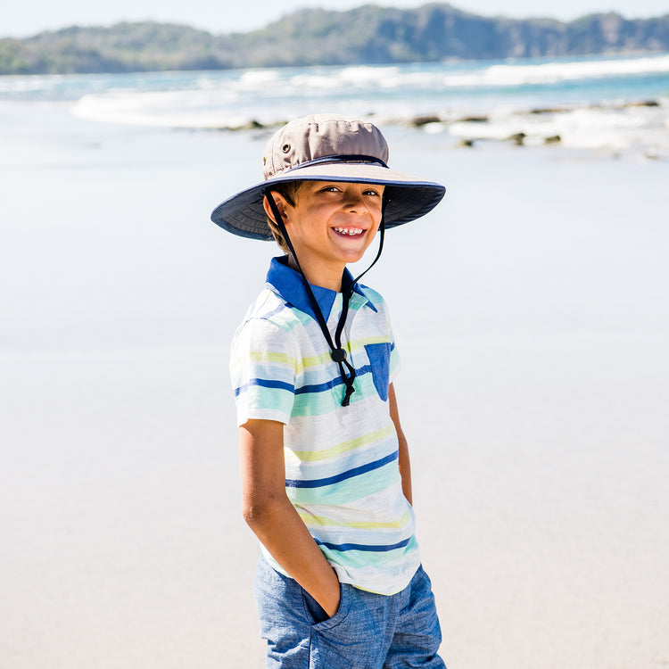 Kid playing on the beach, protected by the Wallaroo Explorer Wide Brim Bucket Sun Hat, designed for active outdoor play and reliable sun safety, Camel/Navy