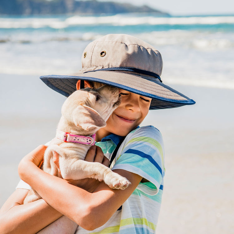 Kid enjoying a sunny beach day, wearing the Wallaroo Children's Explorer Wide Brim Sun Hat, durable UPF 50+ protection during outdoor adventures, Camel/Navy