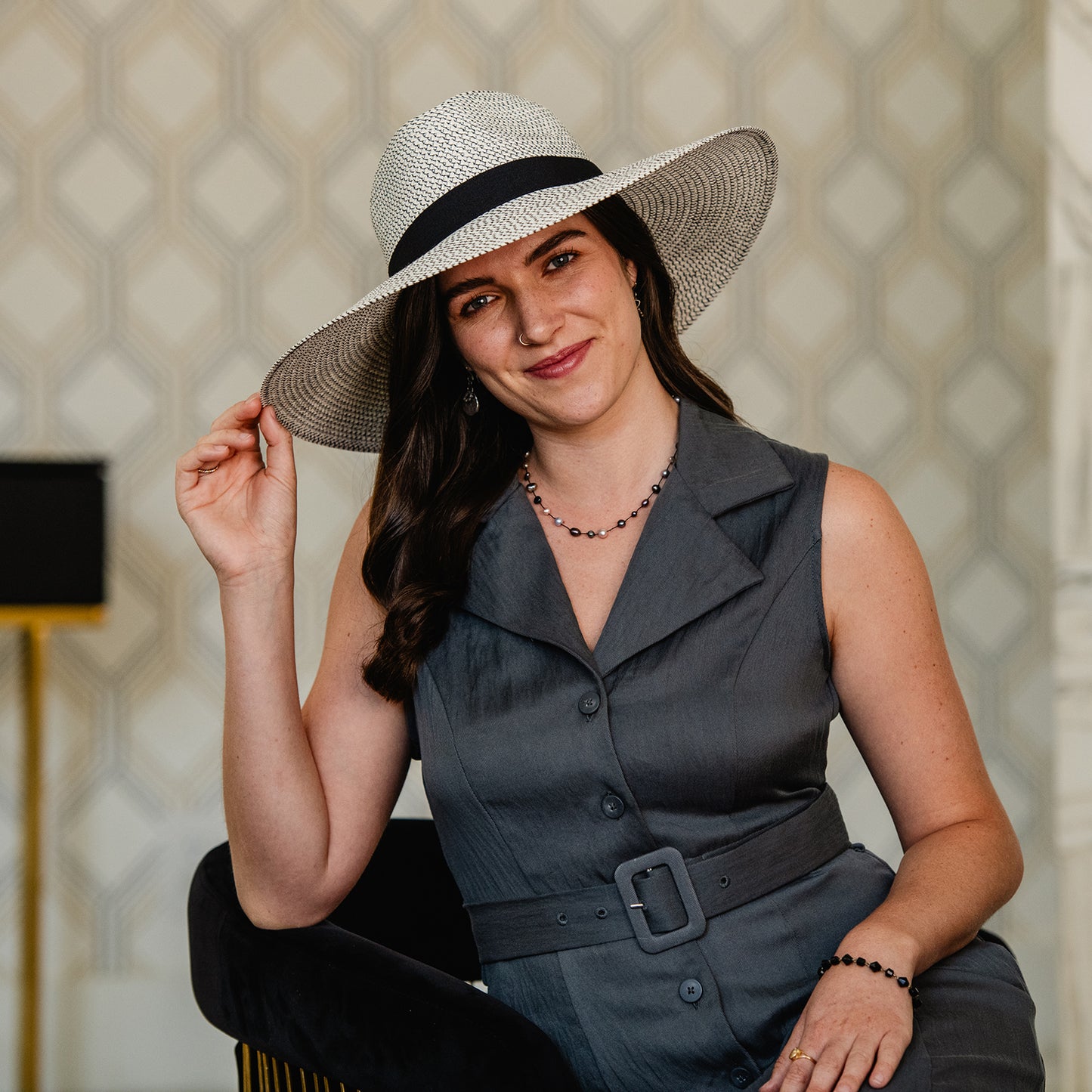 Woman wearing a Carkella Kerrigan wide-brimmed sun hat and gray dress against a patterned wall, Ivory/Black
