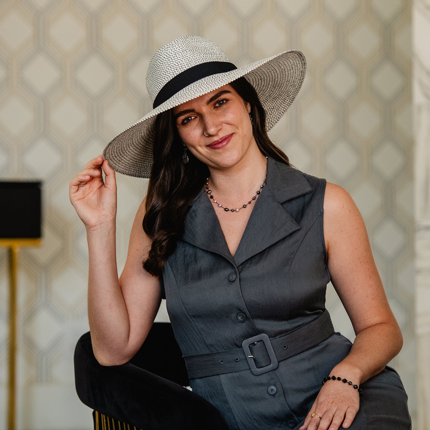 Woman wearing a Carkella Kerrigan wide-brimmed sun hat and gray dress against a patterned wall, Ivory/Black