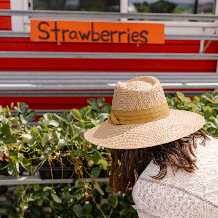 Woman exploring a farmers market in the Wallaroo Klara Sun Hat, combining elegance and practicality with UPF 50+ sun safety and a versatile wide brim, Camel