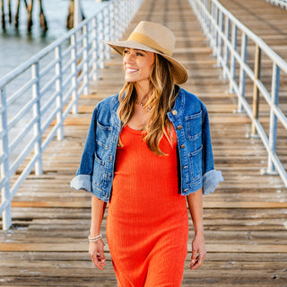 Woman walking along a sunny pier in the Wallaroo Women's Klara Fedora, designed with a wide brim for excellent sun protection and a fashionable look for seaside outings, Camel