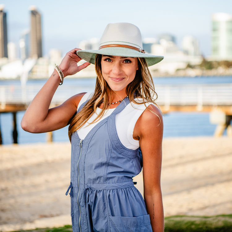 Woman enjoying a sunny day at the beach, wearing the Wallaroo Women's Kristy Wide Brim Fedora Sun Hat, providing UPF 50+ protection and a stylish look for outdoor adventures, Ivory/Sage