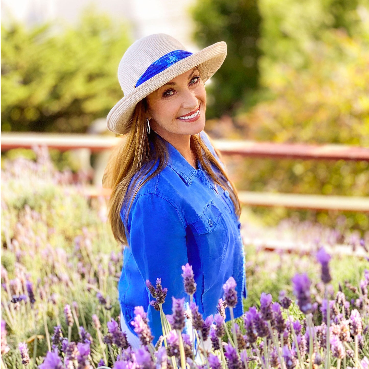 Jane Seymour attending her garden, wearing the Wallaroo Women’s Lady Jane Wide Brim Fedora Sun Hat, with signature artwork on the decorative ribbon trim, providing UPF 50+ protection, White-Beige/Wave