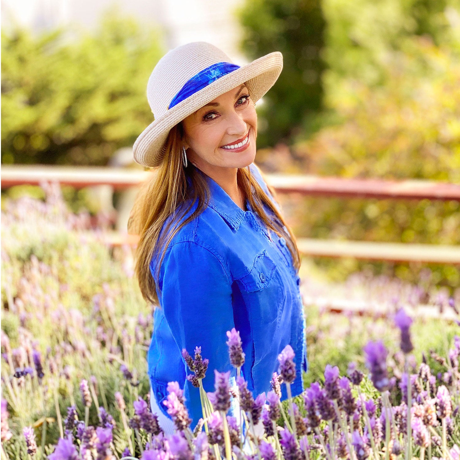 Jane Seymour attending her garden, wearing the Wallaroo Women’s Lady Jane Wide Brim Fedora Sun Hat, with signature artwork on the decorative ribbon trim, providing UPF 50+ protection, White-Beige/Wave