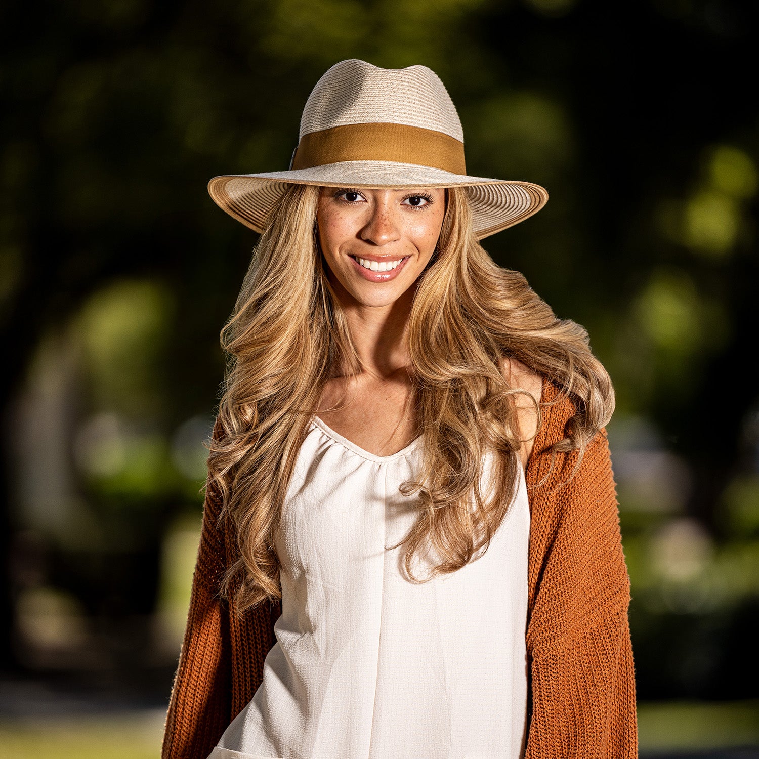 Woman wearing a Carkella Lauren packable hat and brown cardigan with a blurred green background. 