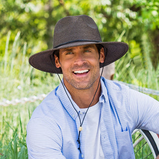 Man attending a family picnic in the park, styled with the Wallaroo Logan Fedora Sun Hat, offering broad sun coverage and a timeless look, Dark Brown