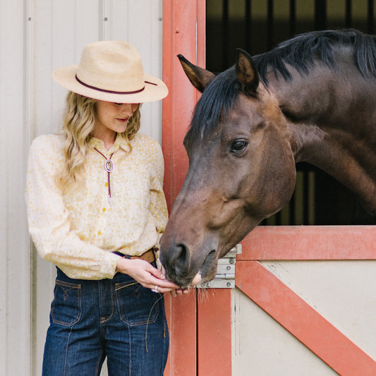 Woman wearing Marina palm fiber sun hat feeding a dark brown horse, Natural