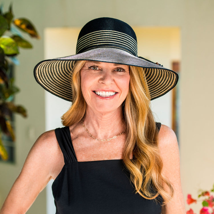 Woman walking through a city park wearing the Wallaroo Marseille Sun Hat, featuring a wide brim and SPF 50+ protection, perfect for stylish outdoor strolls, Black/Natural