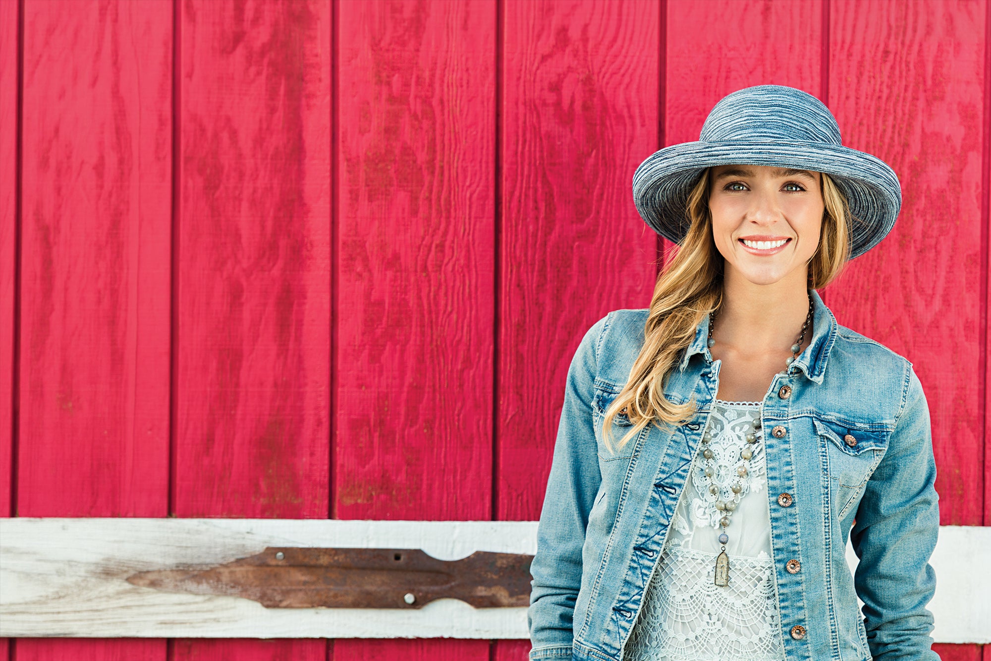 Woman wearing a denim jacket and Sydney hat in front of a red wooden wall