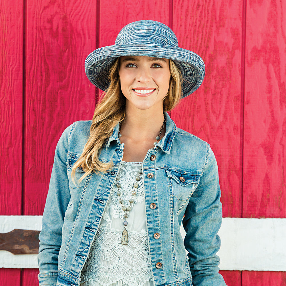 Woman wearing a denim jacket and UPF 30+ Sydney hat in front of a red wooden wall