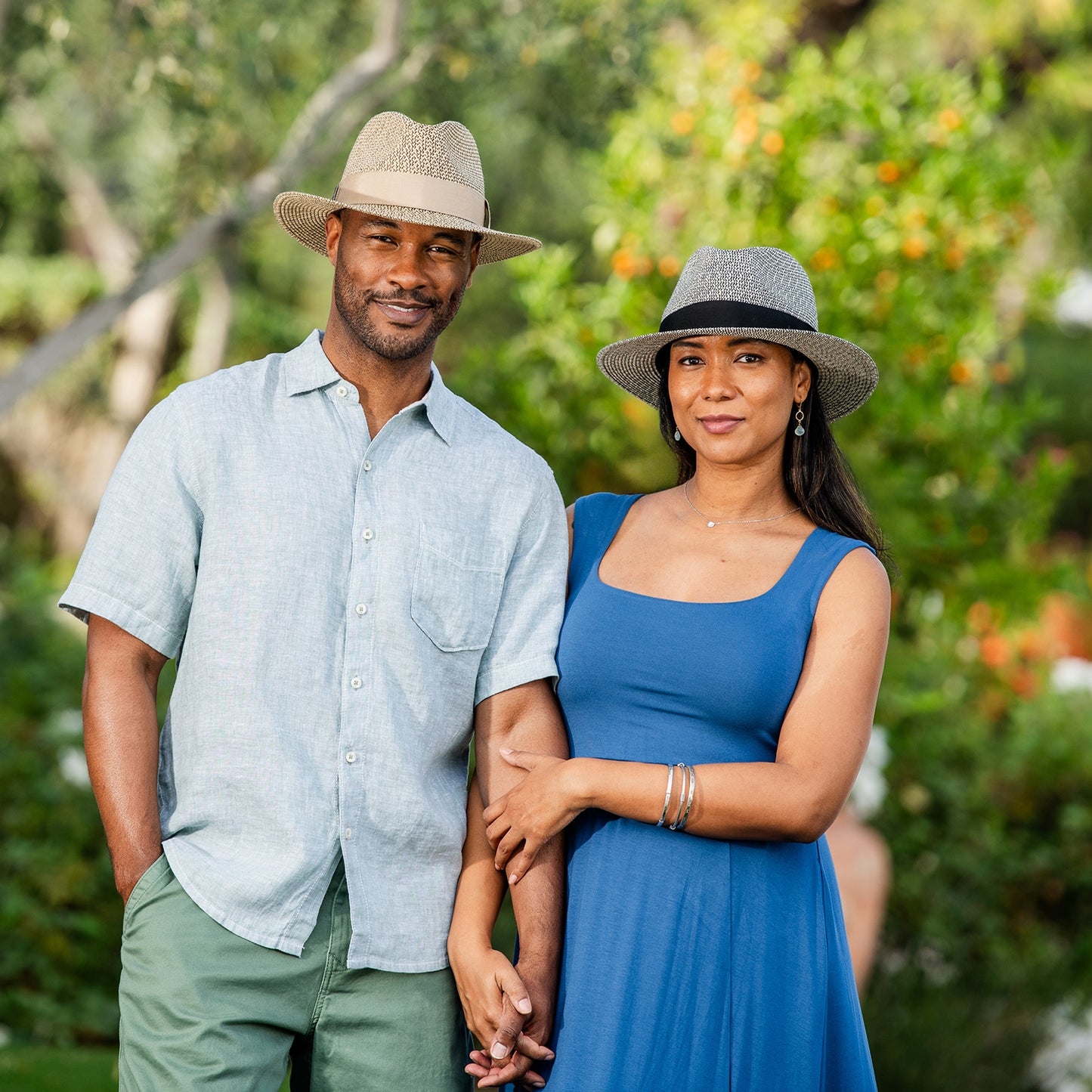 Man and woman standing together wearing Carkella Newhall fedoras outdoors with greenery in the background, Mixed Black and French Beige