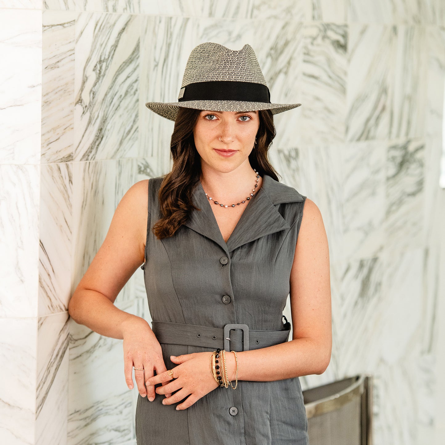Woman wearing a gray sleeveless dress and Carkella Newhall sun hat against a marble wall, Mixed Black