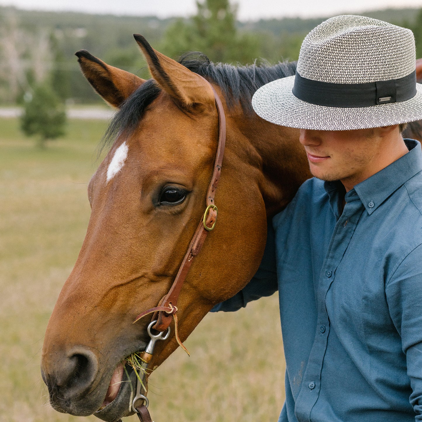 Man wearing Carkella Newhall fedora in a blue shirt and hat standing next to a brown horse in a field, Mixed Black