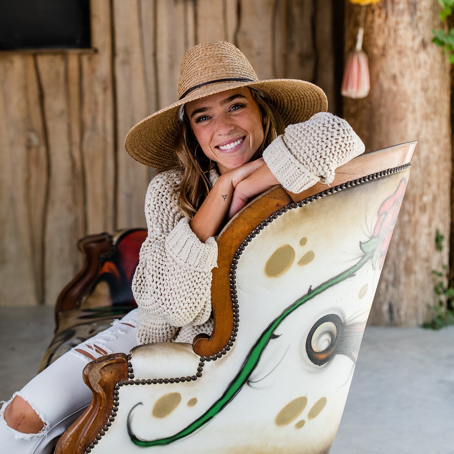Woman wearing Nosara raffia sun hat sitting on a decorative chair with a wooden background