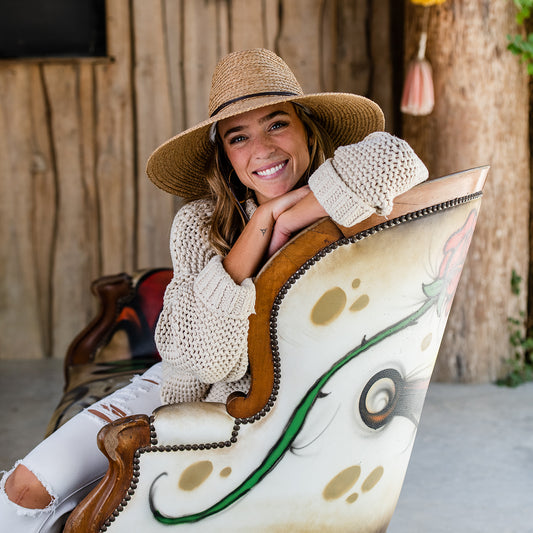 Woman wearing Nosara raffia sun hat sitting on a decorative chair with a wooden background